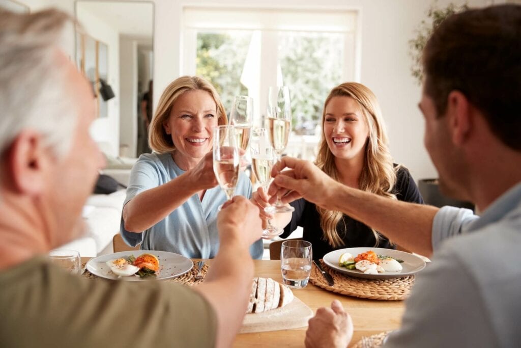 A family of 4 gathered together at the dinner table clinking glasses of champagne together.