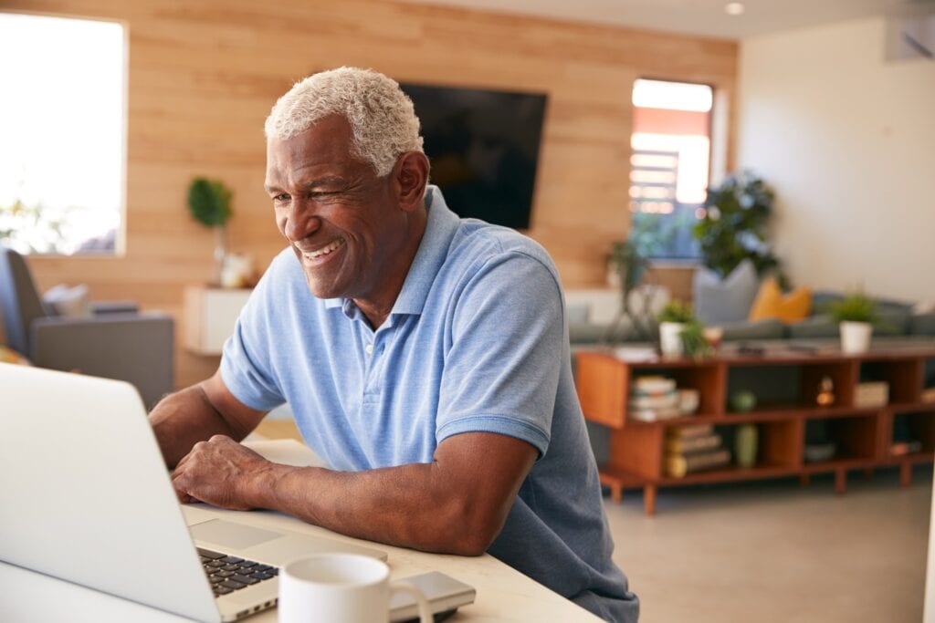 An older man on a laptop smiling with a cup of coffee next to him